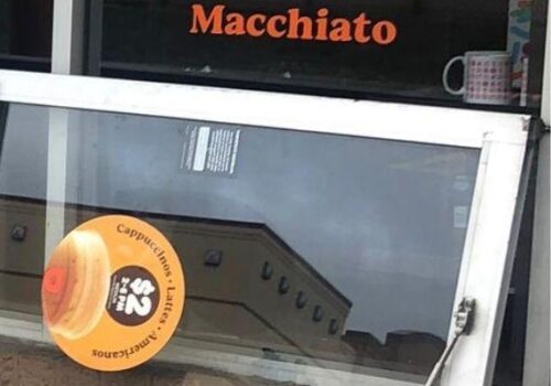 Aluminum glass door with "Macchiato" signage and promotional sticker for cappuccino, showcasing a commercial door installation for a food establishment in Arlington, VA.