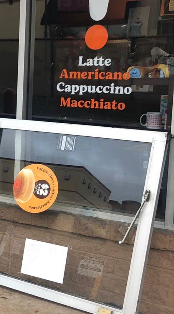 Aluminum glass door with coffee menu featuring "Latte, Americano, Cappuccino, Macchiato" and promotional sticker for $2 drinks, highlighting commercial door installation for food establishments.