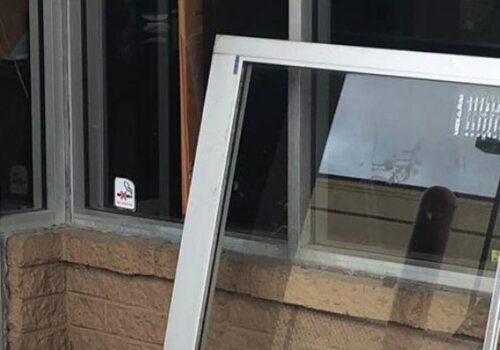 Aluminum glass door installation in progress, showcasing a removed door against a commercial building's window, highlighting door repair services by MacArthur Locks & Doors in Arlington, VA.