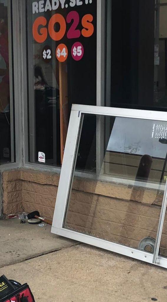 Aluminum glass door installation in front of a commercial establishment, showcasing the door frame on the ground with a colorful promotional sign in the window.