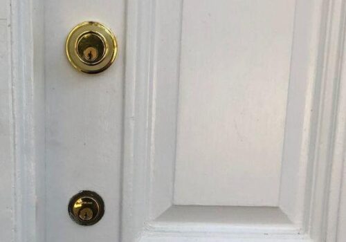 Close-up of a white door featuring a gold doorknob and a deadbolt lock, emphasizing residential security enhancements by MacArthur Locks & Doors.