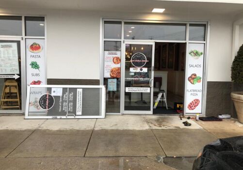 Commercial door installation at a restaurant in Alexandria, VA, featuring signage for pasta, subs, salads, wraps, and flatbread pizza, with a partially removed door and tools on the ground.