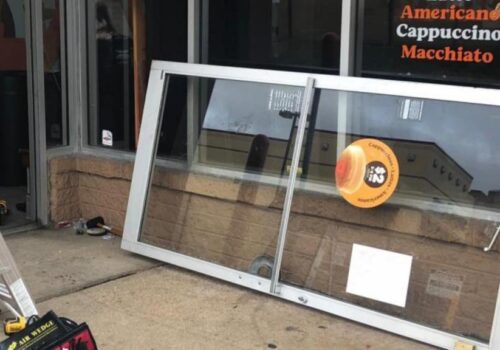 Aluminum glass door installation in progress outside a food establishment, showcasing a partially removed door with tools nearby, emphasizing commercial door repair services by MacArthur Locks & Doors.
