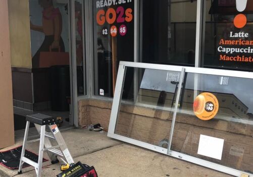 Commercial door installation in progress outside a café, featuring a removed glass door, tools, and a ladder, showcasing MacArthur Locks and Doors' commercial repair services.