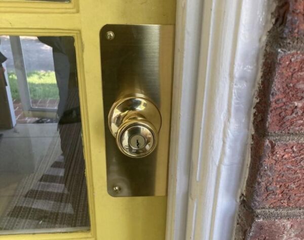 Door knob with brass reinforcer plate installed on a yellow front door, enhancing security for homeowners in Washington, DC.