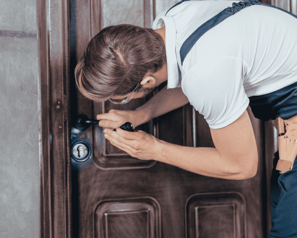 young-manual-worker-in-overall-and-goggles-checking-door-lock-with-flashlight-1