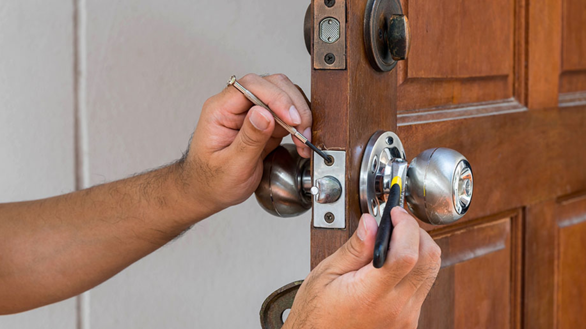 A locksmith is changing the lock on a wooden door.