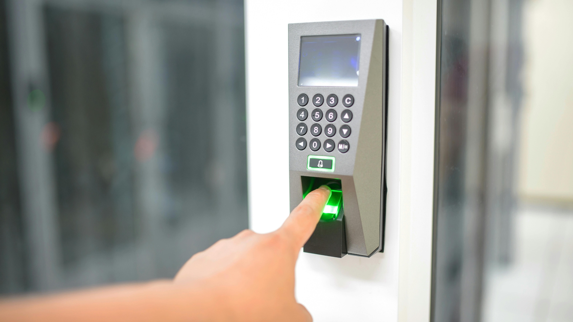 A person using a fingerprint scanner on a keypad door entry system